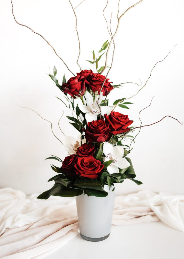 Bouquet "Composition XOXO" avec roses rouges, orchidées, blanches décoratives et verdure dans vase blanc