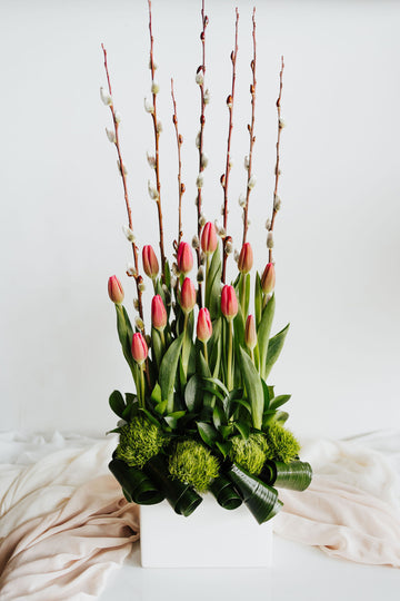 Jardin de Printemps Contemporain avec tulipes roses et feuillage artistique, présenté dans un vase moderne blanc, symbole de fraîcheur et d'élégance printanière.