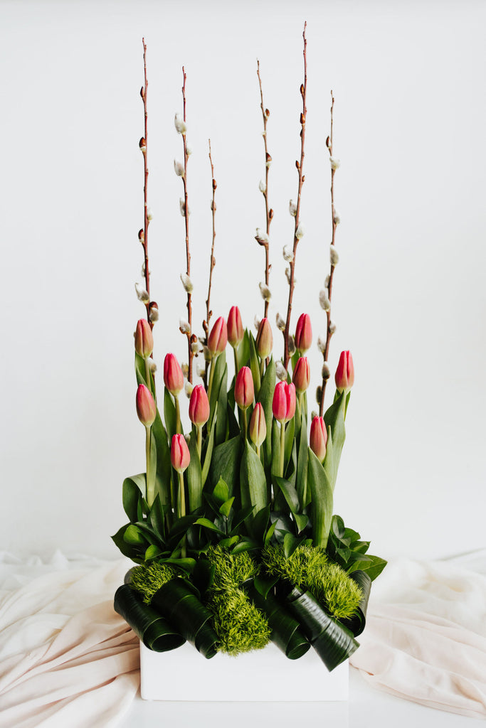 Jardin de Printemps Contemporain avec tulipes roses et feuillage artistique, présenté dans un vase moderne blanc, symbole de fraîcheur et d'élégance printanière.