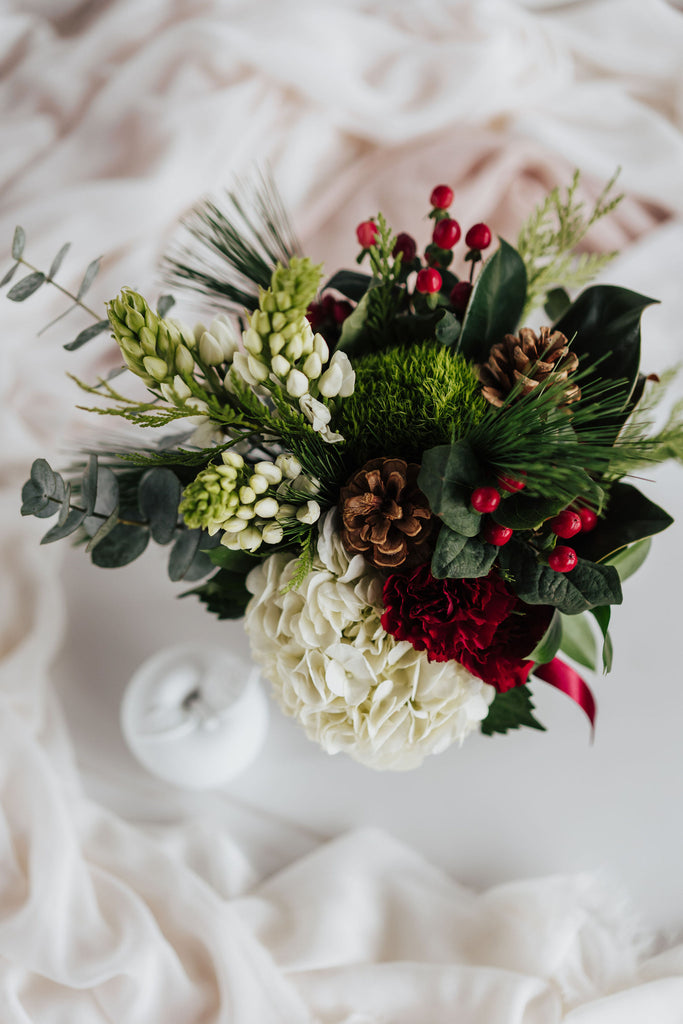 Bouquet nature festive avec hydrangées blanches, baies rouges, conifères et pommes de pin