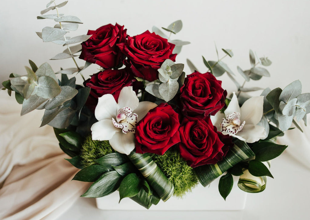 Bouquet "Tendresse" avec roses rouges et orchidées blanches, dans un contenant rectangulaire blanc.