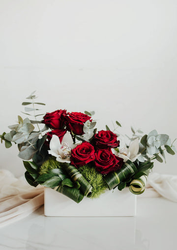 Bouquet "Tendresse" avec roses rouges et orchidées blanches, dans un contenant rectangulaire blanc.